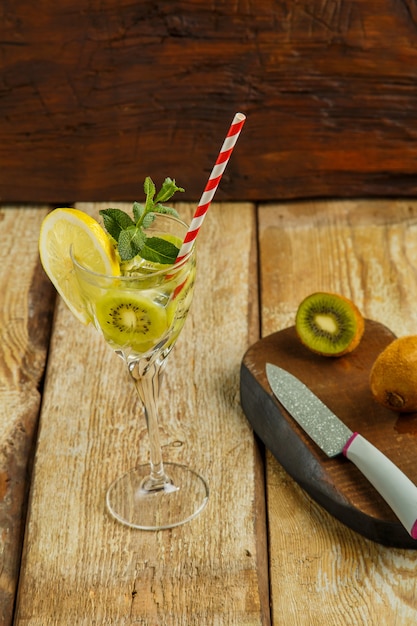 Cocktail à la menthe kiwi et au citron dans un verre sur une table en bois à côté du citron et du kiwi sur une planche