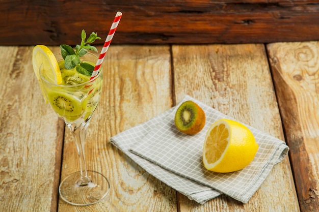 Cocktail à la menthe kiwi et au citron dans un verre sur une table en bois à côté du citron et du kiwi sur une serviette