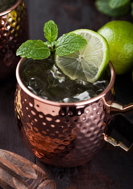 Cocktail mule de Moscou dans une tasse en cuivre avec de la chaux et de la menthe et presse-fruits en bois sur fond de table en bois foncé Macro