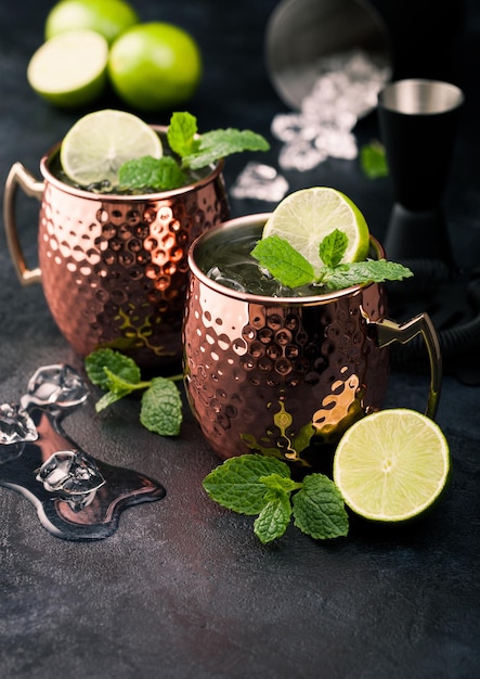 Cocktail de mulet de Moscou dans une tasse de cuivre avec de la chaux et de la menthe et un squeezer en bois sur un fond de cuisine sombre avec des cubes de glace