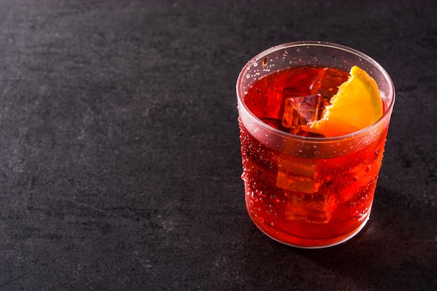 Cocktail Negroni avec morceau d'orange en verre sur fond noir, copyspace
