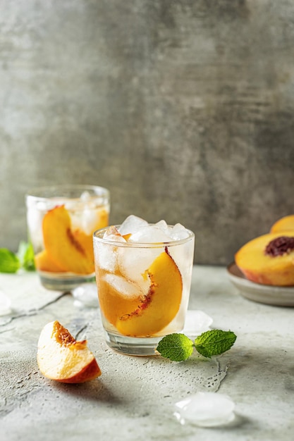 Cocktail de pêche glacé froid avec des tranches de pêche et de menthe sur fond texturé Boisson d'été