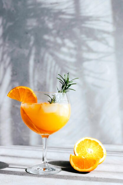 Photo cocktail rafraîchissant avec une orange et une brindille de romarin dans les rayons de la lumière