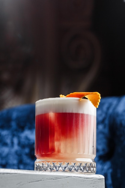 Cocktail rouge classique à l'ancienne dans un verre rétro avec de la glace et du zeste d'orange sur une vue de dessus de fond bleu