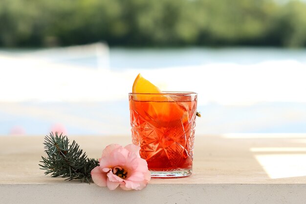 Cocktail rouge dans un verre avec une tranche d'orange. Avec décor de fleurs