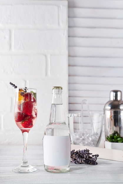 Cocktail rouge avec glace et fraise, lavande avec une bouteille de tonic sur la bouteille sur fond en bois