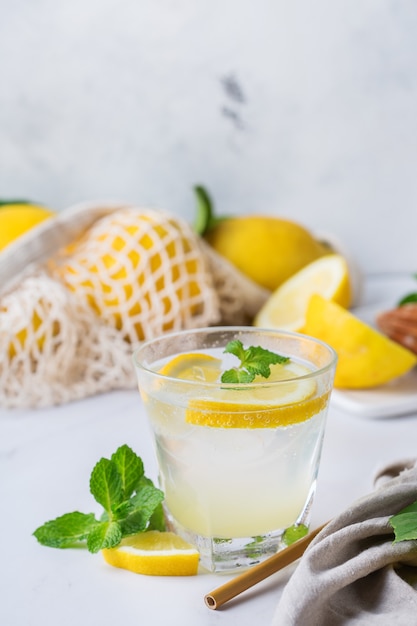 Cocktail de seltz dur avec du citron, de la menthe et de la glace sur une table. Boisson rafraîchissante d'été, boisson avec accessoires tendance zéro déchet, paille de bambou et sac en filet.