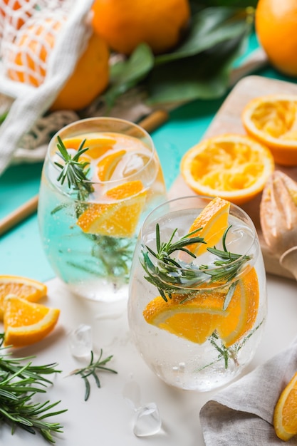 Cocktail de seltz dur à l'orange, au romarin et à la glace sur une table. Boisson rafraîchissante d'été, boisson avec accessoires tendance zéro déchet, paille de bambou et sac en filet.