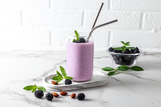 Cocktail ou smoothie aux baies de mûre dans des verres en verre modernes en forme de canette de bière avec de la paille écologique en face d'un mur de briques blanches alimentation saine