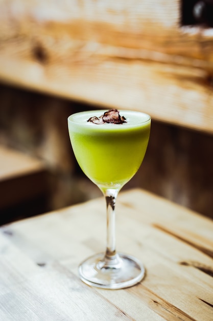 Un cocktail de tequila aigre vert clair dans un verre nick et nora, garniture de chips de radis, sur une table en bois