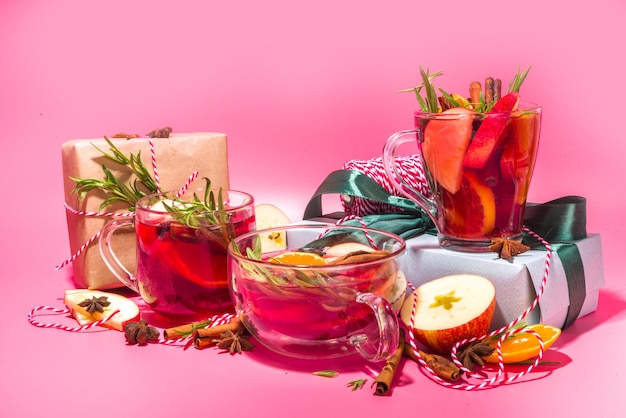 Cocktail de vin chaud maison. Diverses tasses en verre avec du vin chaud épicé chaud d'hiver classique, avec des ingrédients, un décor de Noël et des coffrets cadeaux sur un fond moderne et coloré