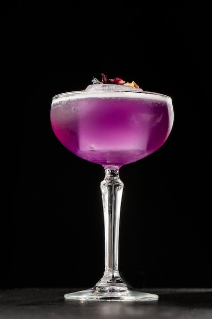 Cocktail violet fait maison avec un grand glaçon sur fond noir