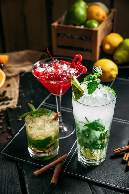 Cocktails alcoolisés frais dans différents verres, mojito cosmopolite et mai tai sur le fond en bois sombre, gros plan, vertical