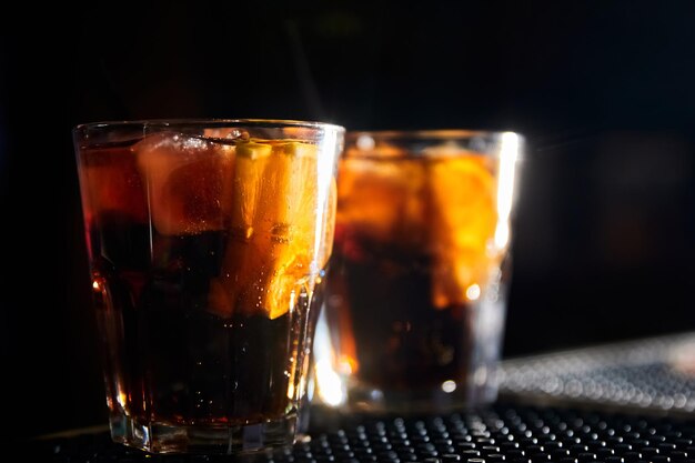 Cocktails alcoolisés avec glace et tranches de citron au bar sur fond sombre
