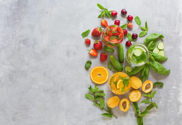 Cocktails de fruits frais d'été Ensemble de boissons d'été sur fond de béton gris Mocktails avec fraise cerise concombre basilic abricot orange et menthe