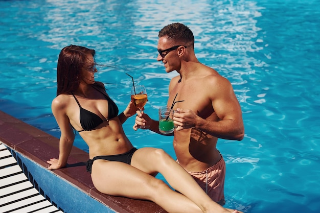 Avec cocktails Joyeux couple ou amis ensemble dans la piscine en vacances