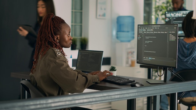 Codeur afro-américain écrivant un langage de programmation sur ordinateur pour développer une nouvelle interface utilisateur. Ingénieur système programmant un script de base de données html dans une agence de développement de logiciels. Prise de vue au trépied.