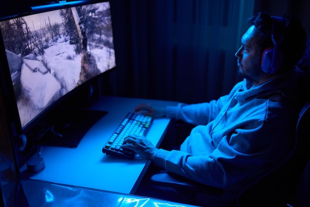 Un codeur travaille tard dans la nuit sur un écran d'ordinateur en codant et en utilisant une application pour smartphone