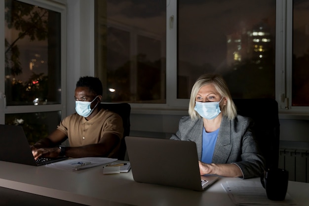 Photo coéquipiers d'affaires travaillant tard au bureau tout en portant des masques médicaux