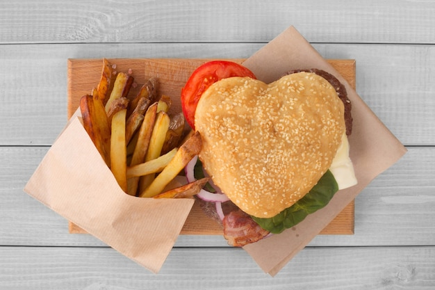 Coeur d'amour hamburger et frites, concept de restauration rapide burger, dîner surprise de la Saint-Valentin, fond en bois, vue de dessus à plat