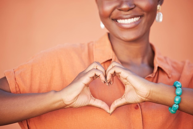 Coeur amour et mains de femme noire pour la beauté soins personnels africains et cosmétiques de mode avec bonheur de paix et sourire avec des dents Fond de mur orange d'été et femme heureuse avec signe d'amour de soi