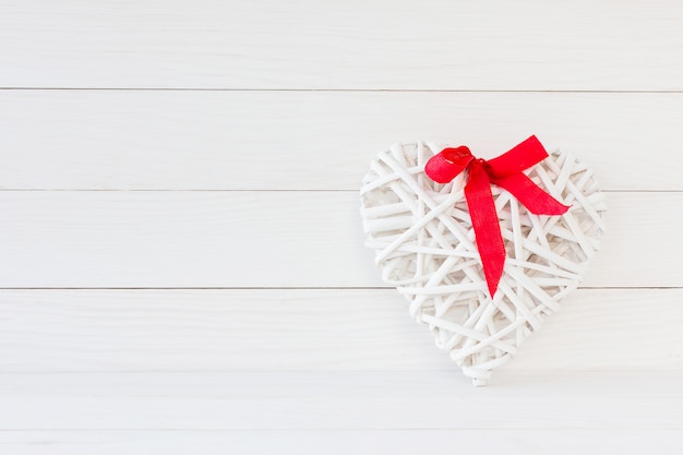 Coeur blanc avec un arc rouge sur un fond en bois blanc. Fond de la Saint-Valentin