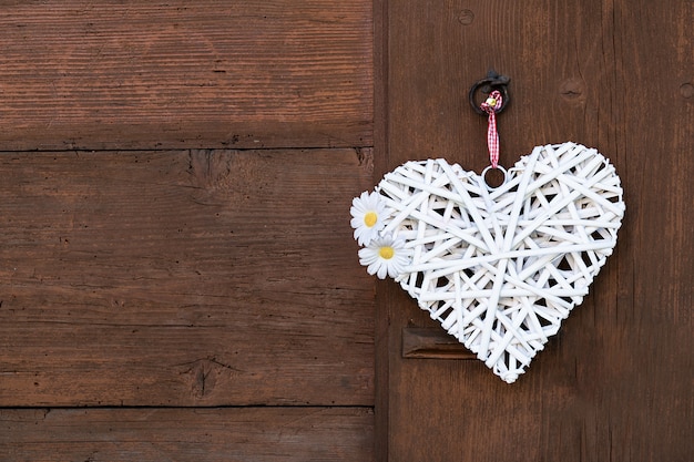 Un coeur blanc tissé avec des marguerites est suspendu à un mur en bois.