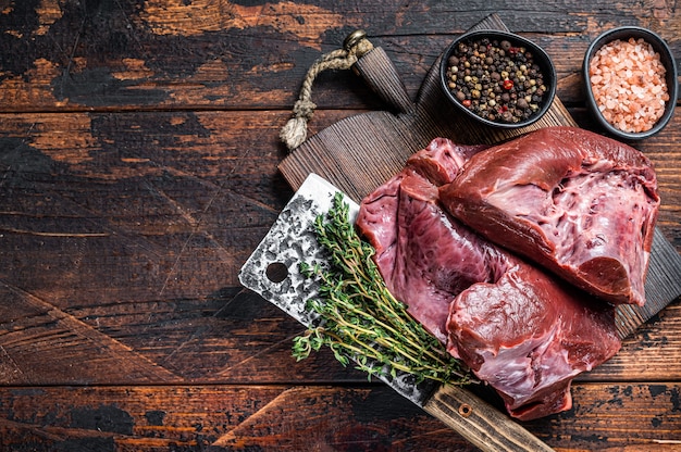 Coeur de boeuf ou de veau tranché cru sur une planche à découper avec un couperet à viande