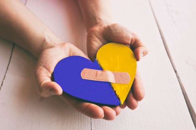 Photo le coeur en bois brisé aux couleurs du drapeau ukrainien dans les mains de la femme