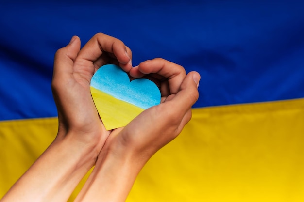 Photo coeur dans les couleurs du drapeau de l'ukraine dans les mains sur le fond du drapeaux mettre fin à la guerre en ukraine aider et soutenir une nation forte bataille pour la justice la liberté et la démocratie