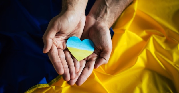 Coeur dans les couleurs du drapeau de l'Ukraine dans les mains sur le fond du drapeaux Mettre fin à la guerre en Ukraine Aider et soutenir une nation forte Bataille pour la justice la liberté et la démocratie