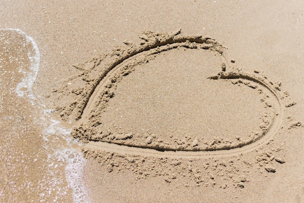Photo coeur dans le sable sur l'océan la mer emportée par une vague