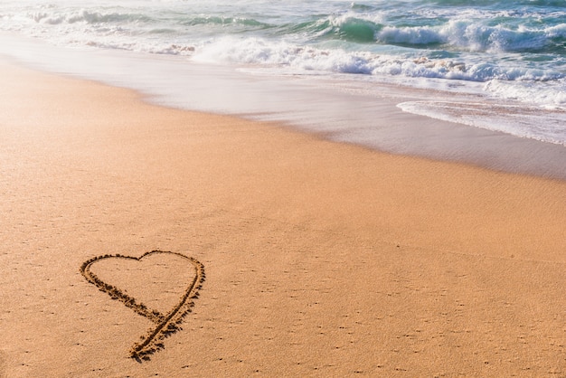 Coeur dessiné dans le sable sur la plage au coucher du soleil avec des vagues qui se lavent