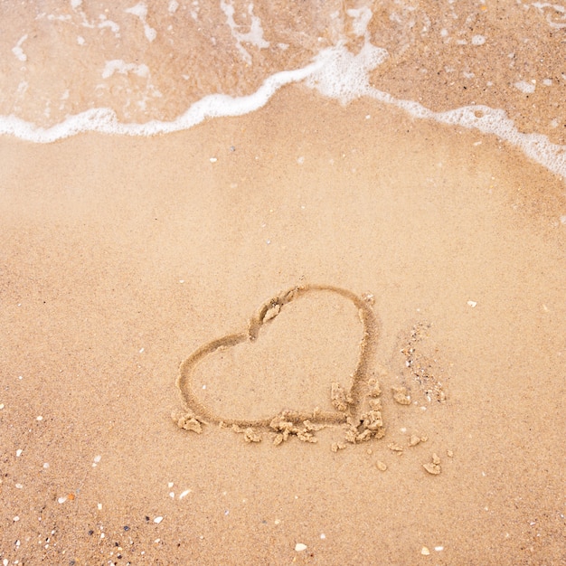 Coeur dessiné dans le sable avec la vague de la mer