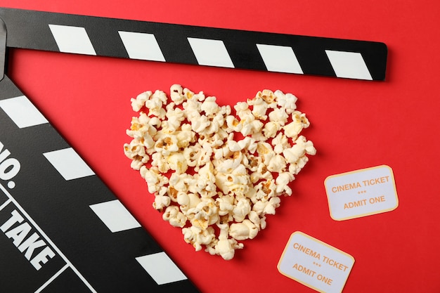 Coeur disposé à partir de pop-corn, clap et billets sur fond rouge