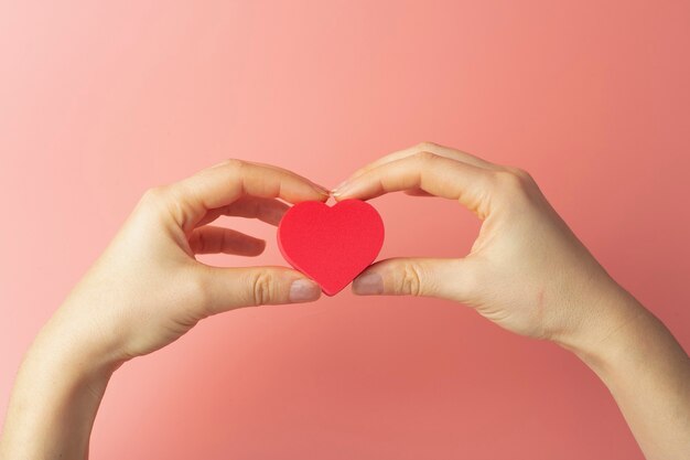 Coeur entre les mains d'une femme sur un fond coloré. Contexte pour la Saint-Valentin (14 février) et l'amour.