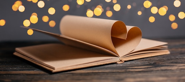 Coeur fait de feuilles de livre dans les lumières, l'amour et le concept de la Saint-Valentin sur une table en bois