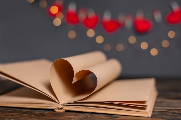 Coeur fait de feuilles de livre dans les lumières, l'amour et le concept de la Saint-Valentin sur une table en bois