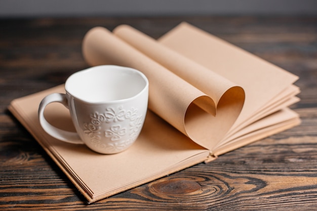 Coeur fait de feuilles de livre avec une tasse, l'amour et le concept de la Saint-Valentin sur une table en bois