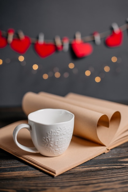 Coeur fait de feuilles de livre avec une tasse dans les lumières, l'amour et le concept de la Saint-Valentin sur une table en bois