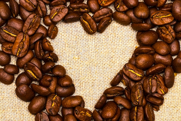 coeur fait avec des grains de café empilés contre une toile de jute.