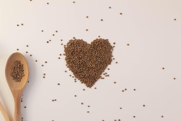 Coeur fait de lentilles crues sur fond blanc avec des ustensiles de cuisine