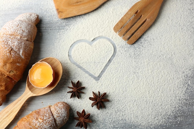 Coeur de farine, croissant et ustensiles de cuisine en bois sur fond gris