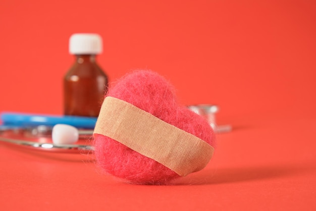 Un coeur en laine naturelle avec un plâtre adhésif collé des médicaments et des outils médicaux sur fond rouge maladies du concept du système cardiovasculaire