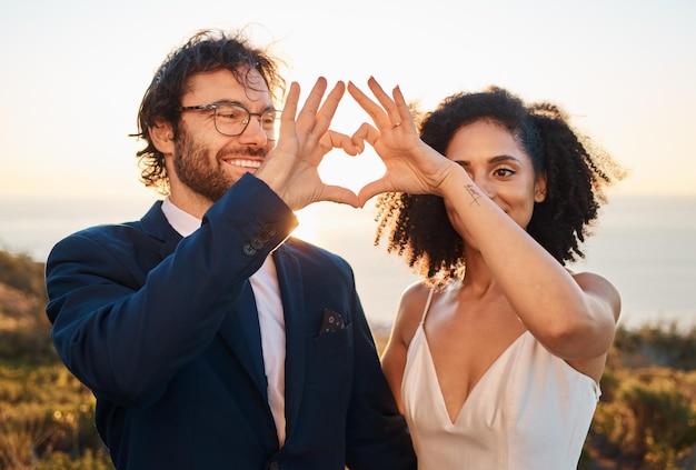 Coeur main signe mariage et couple de mariage dans la nature à la célébration de la confiance et des soins de l'amour Sourire heureux et mariée et homme ensemble en plein air avec bonheur lors d'un événement pour la romance et réservez la date