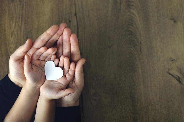 Coeur de papier blanc dans les paumes des enfants et des femmes, vue de dessus. Amour, fête des mères, concept de famille.