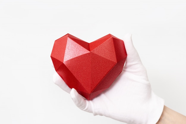 Coeur de papier polygonal rouge à la main avec un gant en tissu blanc