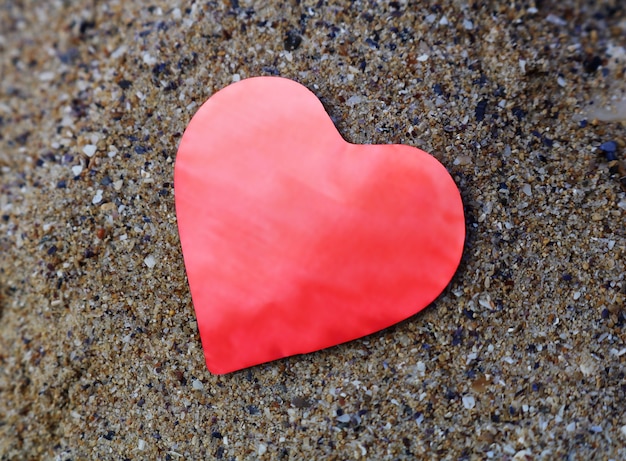 Coeur de papier rouge brillant sur le sable