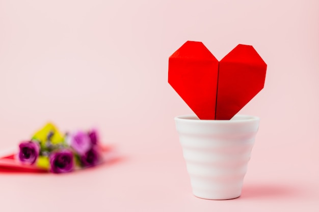 Coeur de papier rouge dans un pot de fleur blanc avec bouquet de roses violettes floues sur fond rose pour l'amour et le concept de la Saint-Valentin