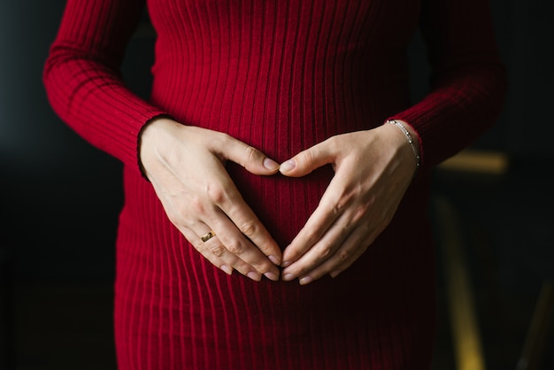 Cœur des paumes en forme de cœur sur le ventre d'une femme enceinte en robe bourgogne